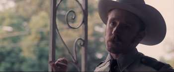 Movie still from “Ain't Them Bodies Saints” (2013), directed by David Lowery – A man with a mustache and a cowboy hat is holding a pen; Close Up shot, Over the shoulder angle