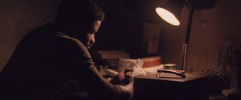 Movie still from “Ain't Them Bodies Saints” (2013), directed by David Lowery – A man sitting at a desk in a dark room; Medium shot, High angle