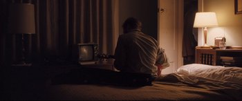 Movie still from “Ain't Them Bodies Saints” (2013), directed by David Lowery – A man sitting in front of a tv playing a guitar; Medium shot, Over the shoulder angle