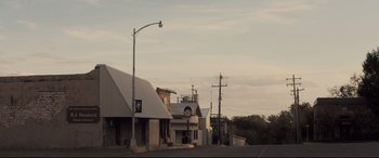Movie still from “Ain't Them Bodies Saints” (2013), directed by David Lowery – An empty street with a clock on the side of the building; Extreme Wide shot, Low angle