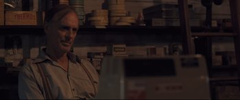 Movie still from “Ain't Them Bodies Saints” (2013), directed by David Lowery – A man standing in front of a shelf with stacks of films; Close Up shot, Over the shoulder angle