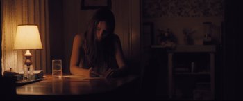Movie still from “Ain't Them Bodies Saints” (2013), directed by David Lowery – A woman sitting at a table writing on a piece of paper; Medium shot, High angle