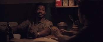 Movie still from “Ain't Them Bodies Saints” (2013), directed by David Lowery – A man sitting at a table with a cup in front of him; Medium shot, Over the shoulder angle