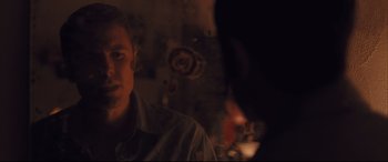 Movie still from “Ain't Them Bodies Saints” (2013), directed by David Lowery – A man sitting in front of a wall with other people; Close Up shot, Over the shoulder angle