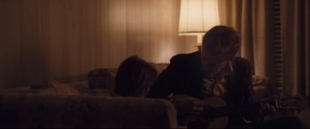 Movie still from “Ain't Them Bodies Saints” (2013), directed by David Lowery – A man and a woman sitting on a couch playing a guitar; Medium shot, Over the shoulder angle
