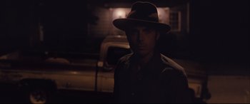 Movie still from “Ain't Them Bodies Saints” (2013), directed by David Lowery – A man wearing a hat standing in the dark; Close Up shot, Over the shoulder angle