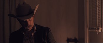 Movie still from “Ain't Them Bodies Saints” (2013), directed by David Lowery – A man wearing a cowboy hat in a dark room; Close Up shot, Over the shoulder angle