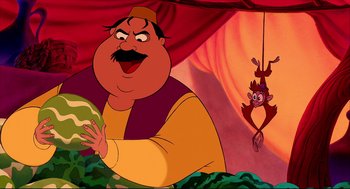 Movie still from “Aladdin” (1992), directed by John Musker – A man holding a watermelon next to a monkey hanging from a rope; Medium shot, High angle