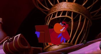 Movie still from “Aladdin” (1992), directed by John Musker – A cartoon of a bird holding an open book in front of a bird cage; Medium shot, Low angle