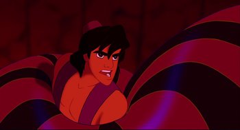 Movie still from “Aladdin” (1992), directed by John Musker – A man with long hair and a hat is sitting on a couch; Medium shot, High angle