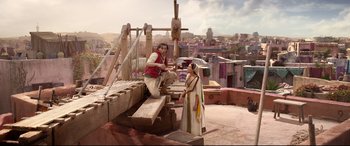 Movie still from “Aladdin” (2019), directed by Guy Ritchie – A man and a woman standing next to each other on top of a building; Wide shot, Low angle