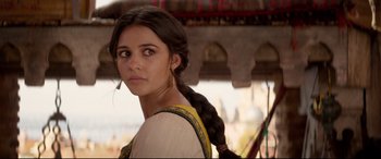 Movie still from “Aladdin” (2019), directed by Guy Ritchie – A young woman with long black hair wearing a yellow and black dress; Close Up shot, Over the shoulder angle