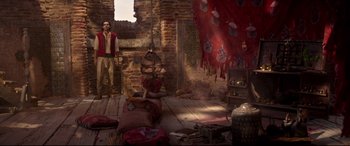 Movie still from “Aladdin” (2019), directed by Guy Ritchie – A man standing in a living room with a fire hydrant in front of him; Wide shot, Overhead angle