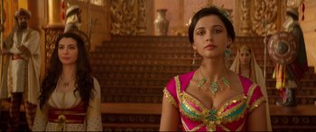 Movie still from “Aladdin” (2019), directed by Guy Ritchie – A woman in a pink and gold dress standing in front of a staircase; Medium shot, Over the shoulder angle
