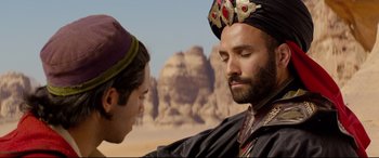 Movie still from “Aladdin” (2019), directed by Guy Ritchie – A man wearing a crown and a turban talking to another man in front of a desert landscape; Close Up shot, Over the shoulder angle