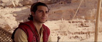 Movie still from “Aladdin” (2019), directed by Guy Ritchie – A man in a red shirt is standing in the desert; Close Up shot, Over the shoulder angle