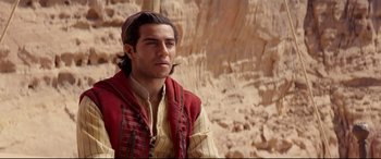 Movie still from “Aladdin” (2019), directed by Guy Ritchie – A man wearing a red vest standing in front of a rock wall; Medium shot, Over the shoulder angle