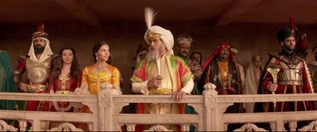 Movie still from “Aladdin” (2019), directed by Guy Ritchie – An old man with a long white beard standing in front of a group of people; Medium shot, Low angle