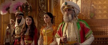 Movie still from “Aladdin” (2019), directed by Guy Ritchie – Two women and an old man standing next to each other; Medium shot, Over the shoulder angle
