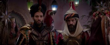 Movie still from “Aladdin” (2019), directed by Guy Ritchie – Two men in costumes with a parrot on their shoulder; Medium shot, Over the shoulder angle