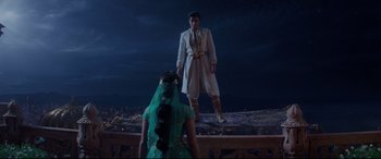 Movie still from “Aladdin” (2019), directed by Guy Ritchie – A man standing on top of a building next to a woman; Wide shot, Over the shoulder angle
