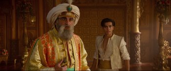 Movie still from “Aladdin” (2019), directed by Guy Ritchie – A man with a beard and a turban standing next to a man with no shirt; Medium shot, Over the shoulder angle