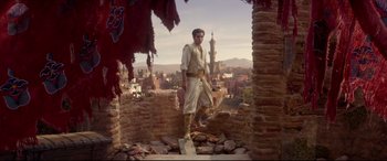 Movie still from “Aladdin” (2019), directed by Guy Ritchie – A man standing on top of a brick wall; Wide shot, Low angle