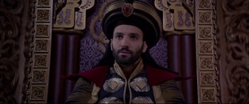 Movie still from “Aladdin” (2019), directed by Guy Ritchie – A bearded man wearing an ornate hat sitting on a throne; Close Up shot, High angle