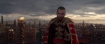 Movie still from “Aladdin” (2019), directed by Guy Ritchie – A man in a red and gold outfit standing in front of a city; Medium shot, Low angle