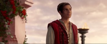 Movie still from “Aladdin” (2019), directed by Guy Ritchie – A man in a red vest looking up at the sky; Medium shot, Over the shoulder angle