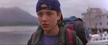 Movie still from “Alaska” (1996), directed by Fraser C. Heston – A young man wearing a hat and a backpack; Close Up shot, Low angle