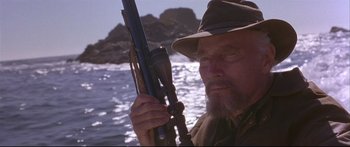 Movie still from “Alaska” (1996), directed by Fraser C. Heston – A man with a beard holding a rifle in front of the ocean; Close Up shot, Low angle