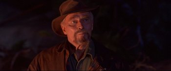 Movie still from “Alaska” (1996), directed by Fraser C. Heston – An older man wearing a brown hat and a brown jacket; Close Up shot, Over the shoulder angle