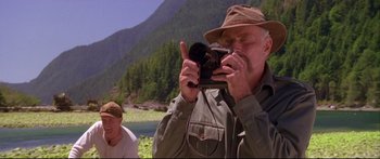 Movie still from “Alaska” (1996), directed by Fraser C. Heston – An older man taking a picture with a camera; Medium shot, Low angle