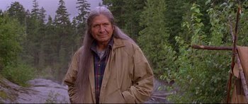 Movie still from “Alaska” (1996), directed by Fraser C. Heston – An older man with long hair standing in front of a forest; Medium shot, Over the shoulder angle