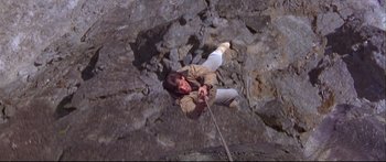 Movie still from “Alaska” (1996), directed by Fraser C. Heston – A man hanging from a rope on top of a mountain; Wide shot, Overhead angle