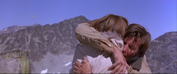 Movie still from “Alaska” (1996), directed by Fraser C. Heston – A man and a woman hugging in front of a mountain; Close Up shot, Low angle