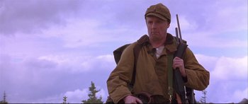Movie still from “Alaska” (1996), directed by Fraser C. Heston – A man in a hat and a jacket is holding a rifle; Medium shot, Low angle