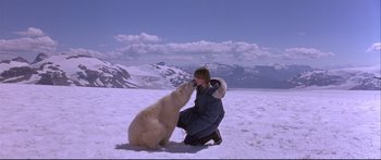 Movie still from “Alaska” (1996), directed by Fraser C. Heston – A woman kneeling down next to a polar bear on top of a snow covered slope; Wide shot, High angle