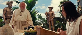 Movie still from “Alexander” (2004), directed by Oliver Stone – A statue of a man holding a whip in front of a table; Medium shot, Over the shoulder angle