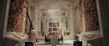 Movie still from “Alexander” (2004), directed by Oliver Stone – A group of people dressed in ancient roman clothing in a room; Extreme Wide shot, High angle