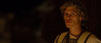 Movie still from “Alexander” (2004), directed by Oliver Stone – A man with long blonde curly hair standing in the dark; Close Up shot, Low angle