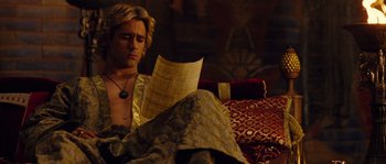 Movie still from “Alexander” (2004), directed by Oliver Stone – A man sitting on a bed reading a paper; Medium shot, Over the shoulder angle