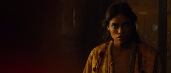 Movie still from “Alexander” (2004), directed by Oliver Stone – A woman in a yellow shirt is standing in a dark room; Close Up shot, Over the shoulder angle