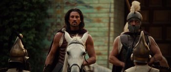 Movie still from “Alexander” (2004), directed by Oliver Stone – A man with long hair is riding a white horse; Medium shot, Over the shoulder angle