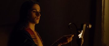 Movie still from “Alexander” (2004), directed by Oliver Stone – A person holding a cell phone while standing in a dark room; Close Up shot, Over the shoulder angle