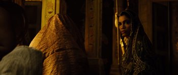Movie still from “Alexander” (2004), directed by Oliver Stone – A woman standing next to a wall in a dark room; Medium shot, Over the shoulder angle
