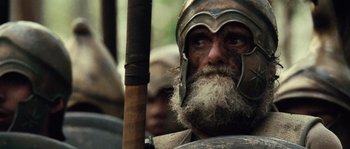 Movie still from “Alexander” (2004), directed by Oliver Stone – An old man with a long beard wearing a helmet and holding a wooden stick; Close Up shot, Low angle