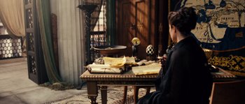Movie still from “Alexander” (2004), directed by Oliver Stone – A woman sitting at a table with papers on it; Medium shot, Over the shoulder angle