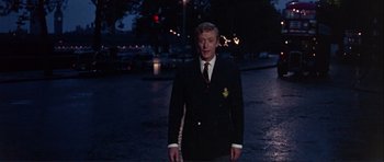 Movie still from “Alfie” (1966), directed by Lewis Gilbert – A man in a suit and tie standing in the middle of the street; Medium shot, Low angle